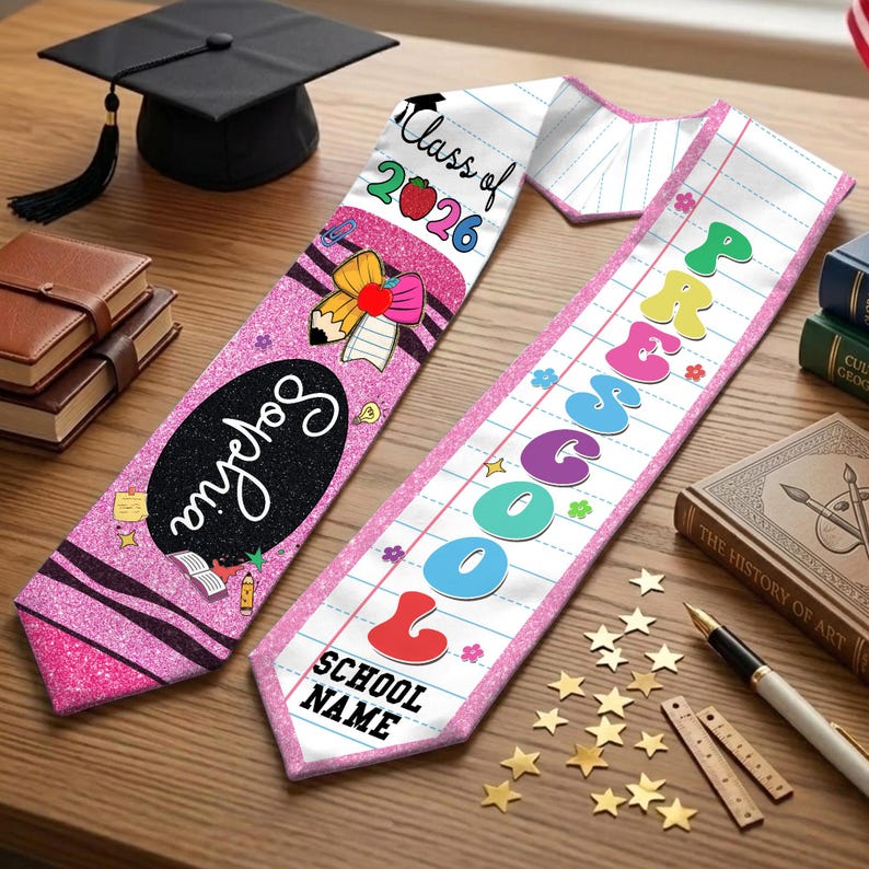 May include: Two graduation sashes with text and graphics, one pink with "Sophia" and "Class of 2026", the other white with "Preschool" and "School Name". A black graduation cap and books are in the background.