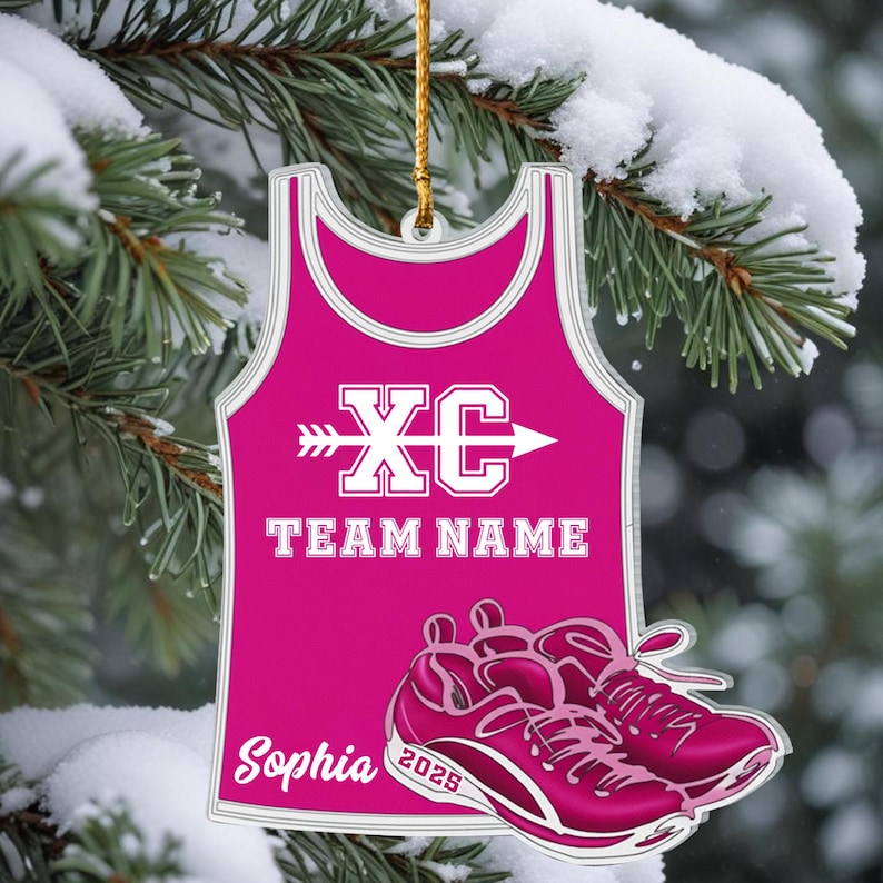 May include: A pink XC team ornament shaped like a tank top, with the text "XC" and "TEAM NAME". Below the tank top are pink running shoes. The name "Sophia" and the year "2025" are also visible.