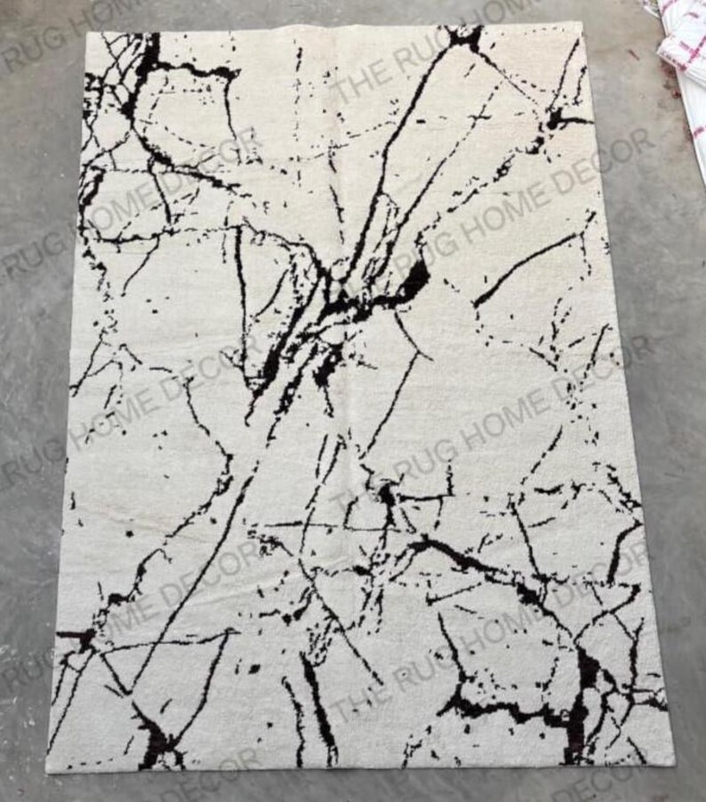 May include: Rectangular area rug with a white background and a black, marble-like pattern. The rug has a textured surface and features the text "THE RUG HOME DECOR" in multiple places.