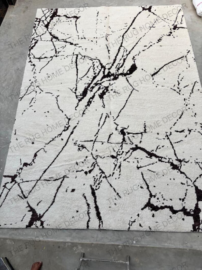 May include: A rectangular, off-white rug with a black, marble-like pattern. The rug's design features dark, irregular lines that create a striking contrast against the lighter background. The rug is a home decor item.