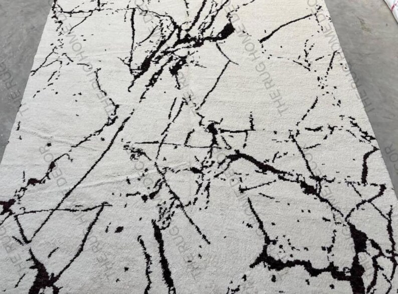 May include: A rectangular white rug with a black marble pattern. The rug's design features irregular black lines and veins across the white surface, creating a natural stone appearance. The rug is a home decor item.