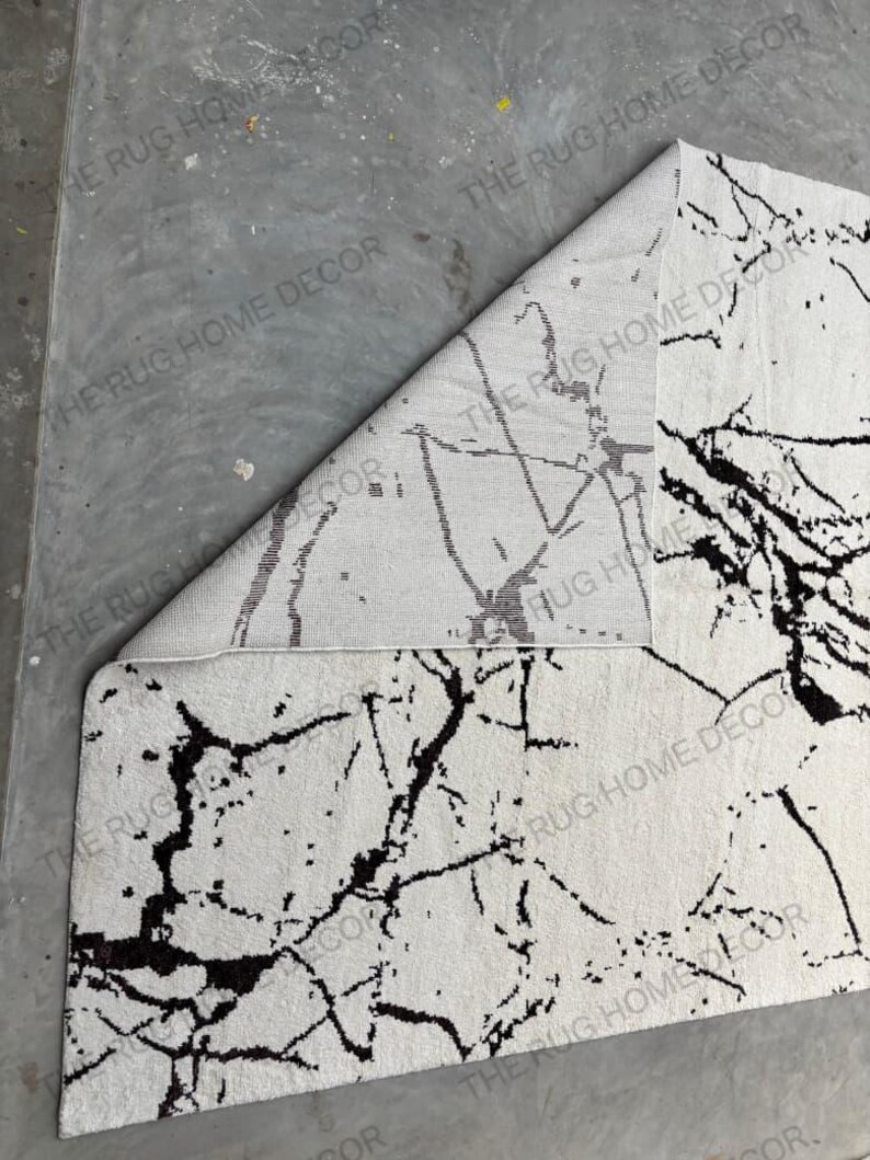 May include: A white rug with a black marble-like pattern. The rug is partially rolled up, revealing the underside, which has a similar but less defined pattern. The rug's design is reminiscent of natural stone.