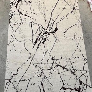 May include: A rectangular rug with a cream-colored background and a striking black marble-like pattern. The design features irregular, vein-like lines that create a dynamic visual texture. The rug is likely made of a soft material.