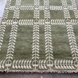 May include: A rectangular green rug with a white leaf pattern. The rug has a grid-like design with vertical and horizontal lines of leaves. The edges of the rug have a fringe.