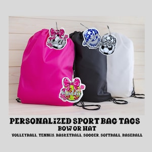 May include: Three drawstring bags with personalized sport bag tags. The tags feature a soccer ball, softball, and a baseball with the names "Maddie" and "Jonathan" on them. The bags are pink, black, and white.