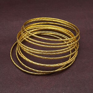 Könnte beinhalten: Ein Stapel goldfarbener Armreifen mit einem strukturierten Design. Die Armreifen sind übereinander gestapelt und in einem kreisförmigen Muster angeordnet.