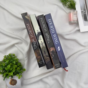 May include: Four hardcover books titled "Fourth Wing" are displayed. The book spines are various colors, including brown, black, and blue, with the title printed vertically. The author's name, "Xaden's POV," is also visible.