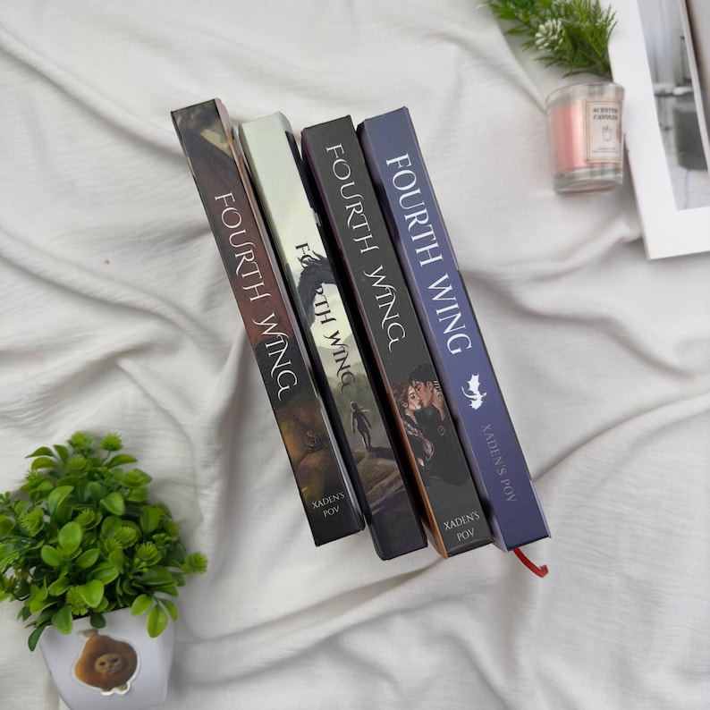 May include: Four hardcover books titled "Fourth Wing" are displayed. The book spines are various colors, including brown, black, and blue, with the title printed vertically. The author's name, "Xaden's POV," is also visible.