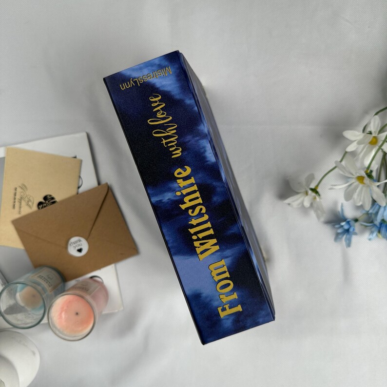 May include: A rectangular box with a navy blue tie-dye pattern and gold text that reads "From Wiltshire with love" and "MistressLynn". The box is angled, with other items like candles and stationary in the background.