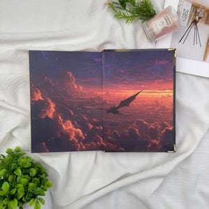 May include: Open book with a fantasy landscape illustration. The artwork depicts a dragon soaring through a sunset sky filled with clouds. The book's interior features a detailed, colorful painting with a dramatic, epic theme.