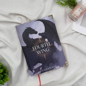 May include: A hardcover book titled "FOURTH WING" with a dragon illustration on the cover. The cover art features a dark dragon with outstretched wings against a purple and gray background. The text "XADEN'S POV" is at the bottom.