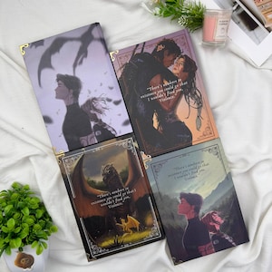 May include: Four fantasy-themed journals with illustrations and quotes. The covers feature couples, a dragon, and figures in a landscape. Each journal has gold corner protectors and a quote from the book "Violence".