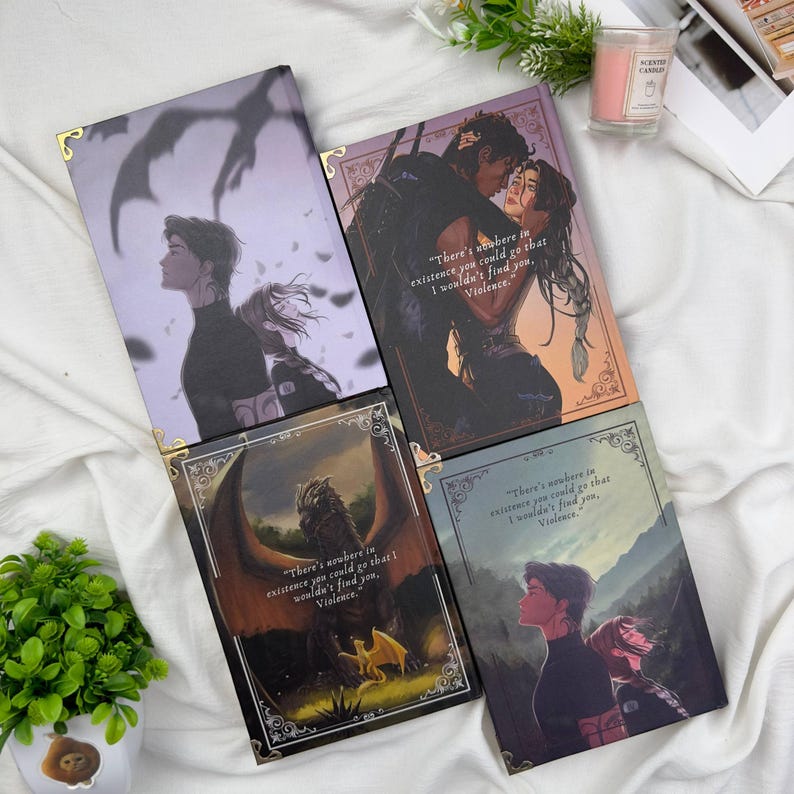 May include: Four fantasy-themed journals with illustrations and quotes. The covers feature couples, a dragon, and figures in a landscape. Each journal has gold corner protectors and a quote from the book "Violence".