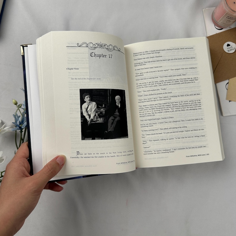 May include: An open book with the text "Chapter 17" on the top of the page. A black and white photo of two people is in the center of the page. The book is held open by a hand.