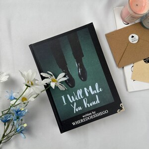 May include: A hardcover book titled "I Will Make You Proud" with a dark green cover featuring an image of legs and dress shoes. The author's name, WHEREDOESSHEGO, is also visible. The book is decorated with white and blue flowers.