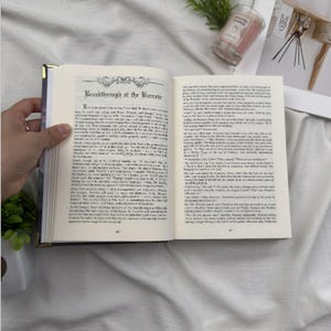 Puede incluir: Un libro abierto con el t&iacute;tulo "Breakthrough at the Burrow" visible. Las p&aacute;ginas est&aacute;n llenas de texto impreso. El libro tiene un borde dorado y est&aacute; abierto por una mano. Una vela perfumada y objetos decorativos est&aacute;n en el fondo.
