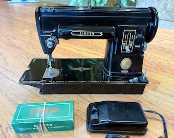 May include: A black Singer sewing machine with gold trim, a stitch length regulator, and a circular emblem. Included are a green rectangular box labeled Singer Sewing Machine Attachments and a black foot pedal with an attached power cord.