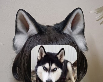May include: A black and white husky dog face is printed on a white card. The card is attached to a black wig with long, straight hair. The wig is on a mannequin head with a brown wooden stand.
