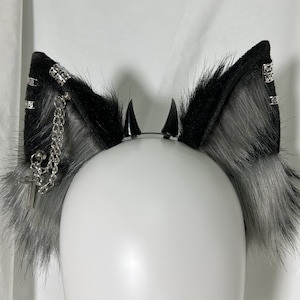 May include: Black and grey faux fur cat ears headband with silver chain and cross charm. The headband has two black spikes on top.
