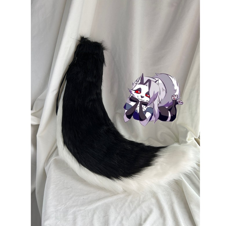 May include: A black and white faux fur tail with a long, fluffy white tip. The tail is curled up on a white surface.