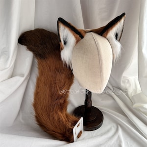 Può includere: Un accessorio per costume di coda di volpe marrone e bianca con una fascia per capelli con un paio di orecchie di volpe. Le orecchie sono fatte di pelliccia morbida e soffice e hanno una punta bianca. La coda è lunga e folta ed è attaccata a una fascia per capelli con una chiusura in velcro.