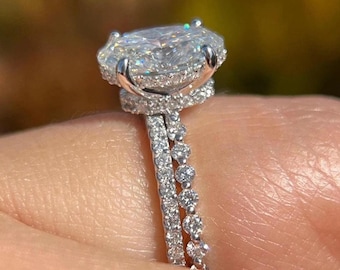Pode incluir: Um close-up de um anel de noivado de diamantes com uma grande pedra central de corte oval. O anel apresenta um halo de diamantes menores ao redor da pedra central e uma banda com diamantes adicionais. O anel é feito de metal prateado.