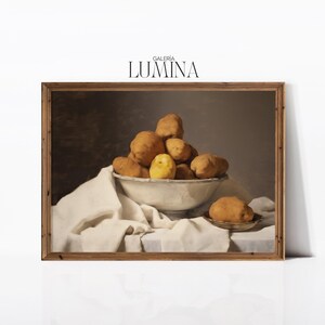 Puede incluir: Una pintura de bodegón con un cuenco lleno de patatas. El cuenco es blanco y se encuentra sobre un mantel blanco. Las patatas son una mezcla de amarillo y marrón. La pintura está enmarcada en un marco de madera marrón.