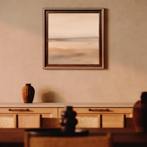 Pode incluir: Uma pintura de paisagem emoldurada com uma moldura de madeira marrom est&aacute; pendurada acima de um arm&aacute;rio de madeira. Um vaso marrom est&aacute; sobre o arm&aacute;rio. A pintura retrata uma cena de praia com cores neutras. A palavra "GALERIA LUMINA" est&aacute; na parte inferior.