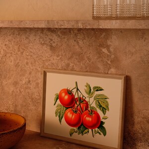 May include: A framed botanical print featuring a cluster of ripe red tomatoes with green leaves. The artwork is set against a neutral background, with a wooden frame. A yellow bowl and clear glasses are also visible.