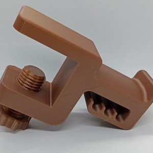 Könnte beinhalten: Eine braune Eckhalterung aus Kunststoff mit einer Gewindeschraube und einer gezahnten Kante. Die Halterung ist so konzipiert, dass sie zwei Materialstücke in einem 90-Grad-Winkel zusammenhält.