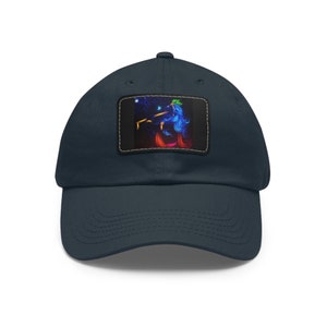 May include: Navy blue baseball cap with a rectangular patch featuring a vibrant illustration of a figure with blue hair and colorful accents. The cap has a curved brim and a classic six-panel design.