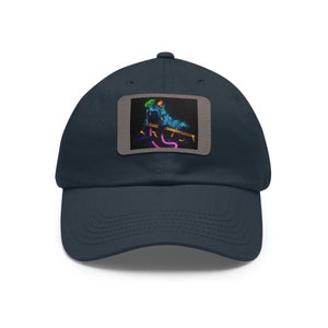 Op de afbeelding: Marineblauwe baseballcap met een rechthoekige patch met een neon illustratie van een figuur die fluit speelt. De figuur is in tinten blauw, roze en goud. De cap is gemaakt van een zachte stof.