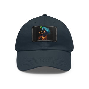 May include: Navy blue baseball cap with a rectangular patch featuring a colorful illustration of a figure playing a flute. The figure has blue hair and is set against a black background. The cap is made of a soft material.