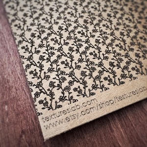 Op de afbeelding: Close-up van een lasergesneden houten plaat met een bloemenpatroon. Het ontwerp toont delicate zwarte bloemen en stelen. De tekst "textureslab.com" en "www.etsy.com/shop/textureslab" is zichtbaar.