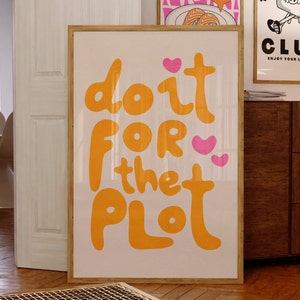 May include: A framed print with a pink background and orange text that reads "do it for the plot". There are two pink hearts on the print.