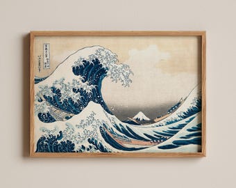 Op de afbeelding: Een ingelijste print van De Grote Golf bij Kanagawa met een grote donkerblauwe brekende golf, drie houten boten met roeiers en de verre berg Fuji tegen een beige lucht. Het kunstwerk bevat verticale Japanse tekst in de linkerbovenhoek.
