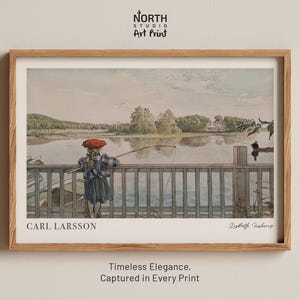 Può includere: Una stampa artistica incorniciata con un acquerello di una persona che pesca da un molo di legno. L'opera d'arte, di Carl Larsson, raffigura una serena scena lacustre con una persona con un cappello rosso. La stampa è in una cornice di legno. Il testo recita "North Studio Art Print".