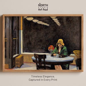 May include: A framed art print featuring a painting of a person in a yellow hat and green coat sitting at a round table in a dark cafe. The person holds a small white cup. A bowl of fruit sits on the table. The text North Studio Art Print appears above.