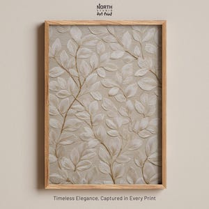 May include: A rectangular wall art print in a light wood frame featuring a textured beige background with a repeating pattern of embossed white leaves and thin brown stems. The text North Studio Art Print appears above and Timeless Elegance, Captured in Every Print below.