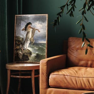 a painting of a woman standing on a cliff, with a stormy sea in the background. The painting is displayed on a wooden table, and there is a brown leather couch in the background.