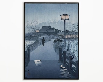 May include: A vertical woodblock print in shades of blue and grey depicting a rainy evening scene. A lone figure with an umbrella walks across a bridge toward traditional buildings. A tall lantern stands on the right, illuminating the path.