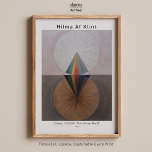 Könnte beinhalten: Ein gerahmter Kunstdruck von Hilma Af Klints Werk Group IX/SUW, The Swan No. 12, 1915. Das Bild zeigt eine zentrale rautenförmige Figur in Regenbogenfarben, platziert zwischen einem hellen oberen Kreis und einem braunen unteren Kreis in einem hellen Holzrahmen.