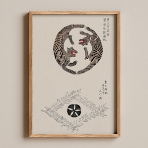 May include: A framed print on a light beige background featuring two black tigers with red mouths arranged in a circular pattern at the top and a central black circular emblem surrounded by stylized black leaf-like shapes at the bottom with Japanese text.