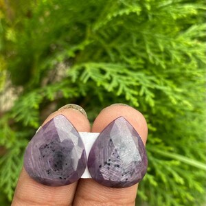 May include: Two pear-shaped purple gemstones with a faceted cut and a sparkly finish.