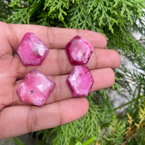 Może przedstawiać: Cztery różowe, fasetowane kaboszony z kamieni szlachetnych. Kaboszony mają kształt sześciokąta o zaokrąglonych krawędziach. Kaboszony są ułożone w rzędzie na dłoni.