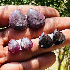 Op de afbeelding: Vier peervormige edelstenen met een dieprode kleur en zwarte insluitsels. De edelstenen zijn gefacetteerd en hebben een hoge glans.