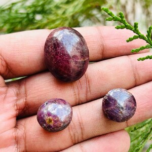 May include: Three red ruby gemstones, one oval shaped and two round, with a sparkly, iridescent finish.