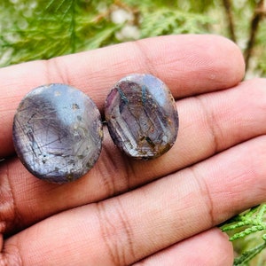 May include: Two round, purple and gray gemstone cabochons with a starburst pattern. The cabochons are about 1 inch in diameter.