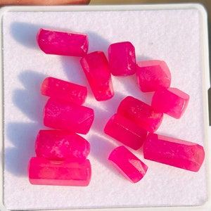 May include: A collection of ten pink gemstones, cut into rectangular shapes, displayed on a white surface.
