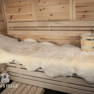 Könnte beinhalten: Ein weißer Schaffellteppich, der auf einer Holzsaunabank ausgelegt ist. Der Teppich ist weich und flauschig und wäre perfekt, um jeder Sauna einen Hauch von Luxus zu verleihen.